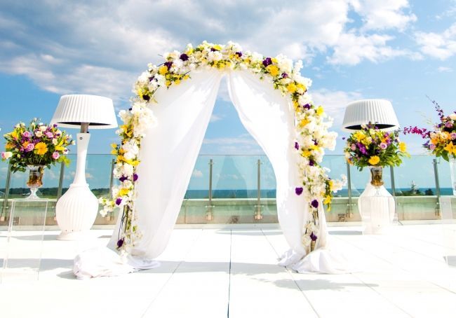 A wedding altar created using floral arrangements and draped white cloth, at High Park Terrace with a view of Lake Ontario.