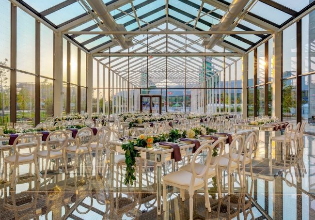 A banquet set-up with elegant white furniture and floral arrangements, for an event in New Fort Hall which is a glass-enclosed space.
